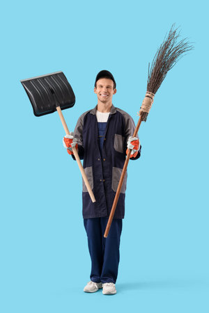Male scavenger with snow shovel and broom on blue background