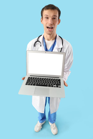 Surprised male doctor with blank laptop on blue backgroundの写真素材
