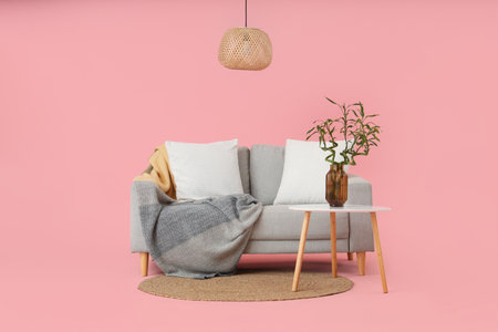 Table with bamboo stems in vase, sofa and lamp on pink backgroundの写真素材
