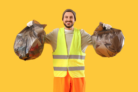 Male scavenger with full garbage bags on yellow backgroundの写真素材