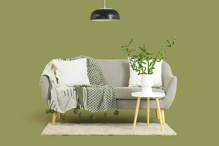 Table with bamboo stems in vase, sofa and lamp on green backgroundの写真素材
