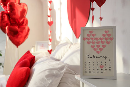 Calendar with hearts and marked date 14 FEBRUARY on bedside table in festive bedroom, closeup. Valentine's Day celebrationの写真素材