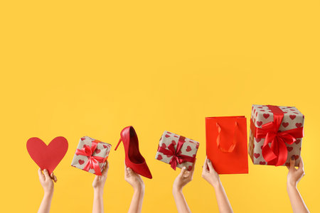 Female hands with heart, gift boxes, bag and high heel on yellow background. Valentine's Day celebrationの写真素材