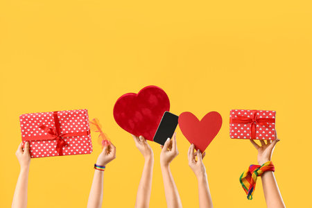 Female hands with gift boxes, heart and mobile phone on yellow background. Valentine's Day celebrationの写真素材