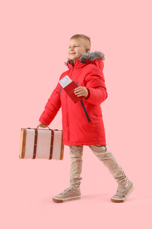 Cute little boy in puffer jacket with suitcase and passport on pink background. Travel conceptの写真素材