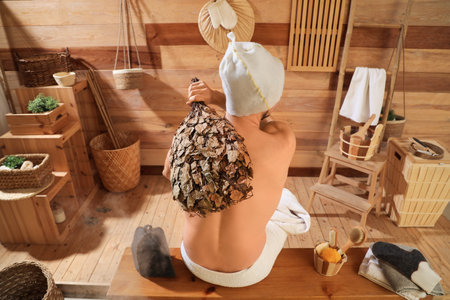 Young man with whiskey relaxing on bench in sauna, back viewの写真素材
