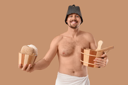 Handsome man with sauna supplies on beige backgroundの写真素材