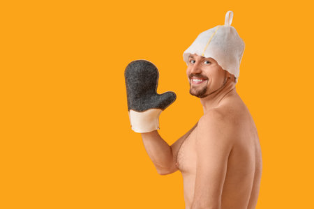 Handsome man in sauna felt hat with massage glove on yellow backgroundの写真素材