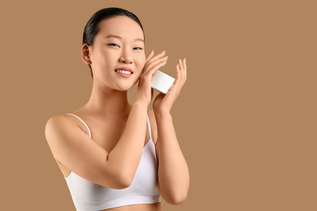 Young Asian woman with jar of cream on beige backgroundの写真素材
