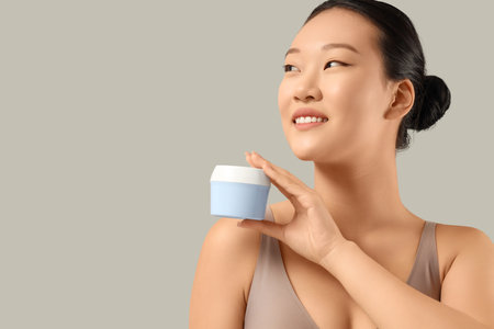 Young Asian woman with jar of cream on gray background, closeupの写真素材