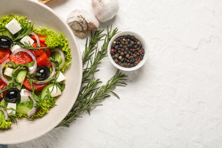 Bowl with tasty Greek salad, spices and rosemary on light backgroundの写真素材