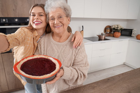 Young woman and her grandmother with tasty pie taking selfie in kitchenの写真素材