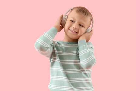 Cute little boy in headphones listening to music on pink backgroundの写真素材