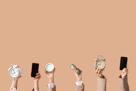Female hands with alarm clocks, mobile phones and eyeglasses on beige background. Time management conceptの写真素材