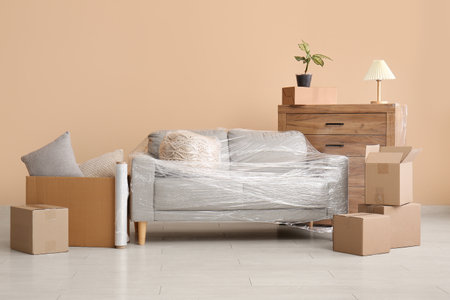 Wrapped sofa with stretch film and cardboard boxes in living room on moving dayの写真素材