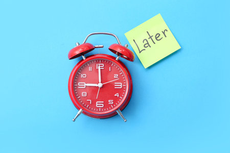 Alarm clock and sticky note with word LATER on color background