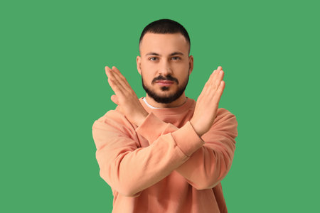Young man showing STOP gesture on green background. Rules conceptの写真素材