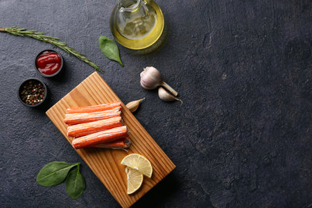 Wooden board with tasty crab sticks and different spices on dark backgroundの写真素材