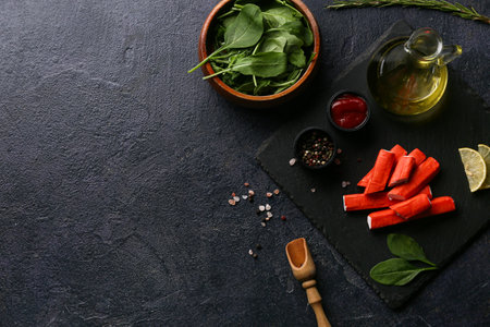 Black board with tasty crab sticks and different spices on dark backgroundの写真素材
