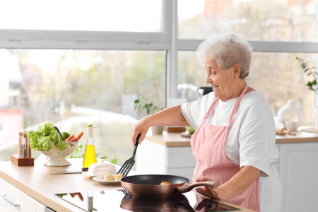 Senior woman putting fried cottage cheese pancakes on plate in kitchenの写真素材