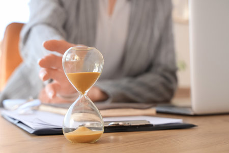 Businesswoman with hourglass on desk in office, closeupの写真素材