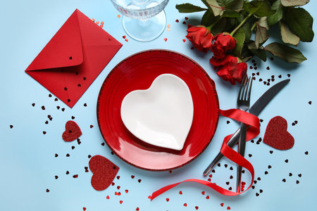 Beautiful table setting with envelope and red roses on blue background. Valentine's Day celebrationの写真素材
