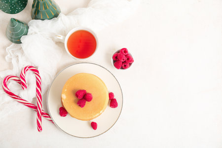 Plate of sweet pancakes with berries, Christmas candy canes and cup of tea on white backgroundの写真素材