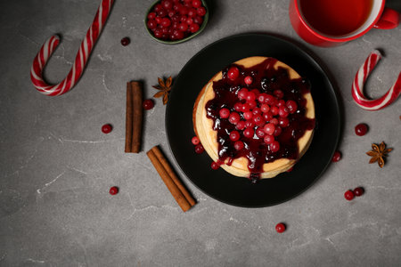 Plate of sweet pancakes with red currants, Christmas candy canes and cup of tea on gray backgroundの写真素材
