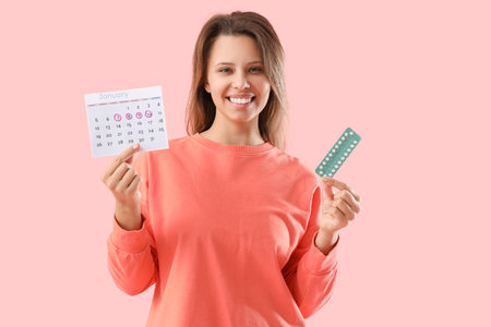 Young woman with menstrual calendar and pills on pink backgroundの写真素材