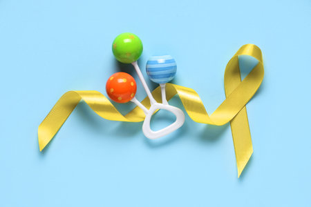 Baby rattle with yellow ribbon on color background. Childhood cancer awareness conceptの写真素材