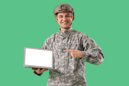 Young soldier pointing at blank laptop on green backgroundの写真素材