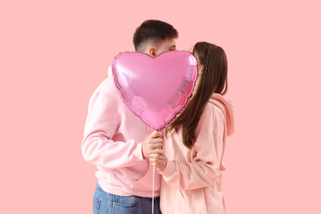 Young couple in love with balloon kissing on pink background. Valentine's Day celebrationの写真素材