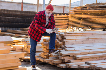 Happy mature male carpenter with tablet at sawmillの写真素材