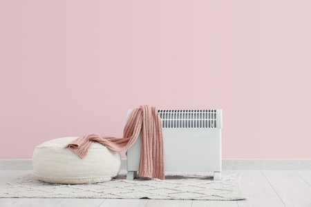 Modern convector heater with warm scarf and pouf near pink wallの写真素材