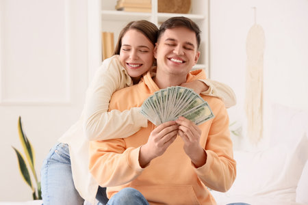 Happy young woman hugging her boyfriend with money in bedroomの写真素材