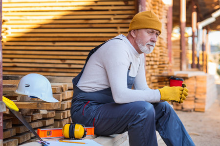 Mature male carpenter with cup of coffee sitting at sawmillの写真素材