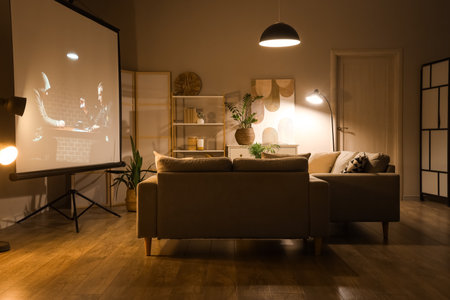 Interior of dark living room with projector screen, sofas and glowing lamps at nightの写真素材