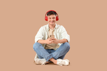 Young man in headphones using mobile phone on beige backgroundの写真素材