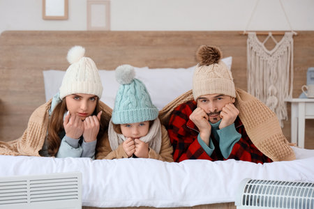 Frozen family lying near electric convector heaters in bedroomの写真素材