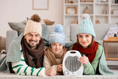 Frozen family with electric fan heater lying on floor at homeの写真素材