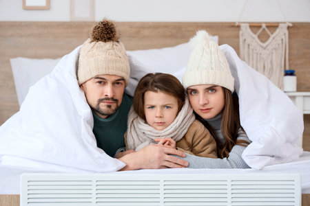 Frozen family with lack of heating lying under blanket in bedroomの写真素材
