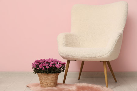 Wicker basket with chrysanthemum flowers on carpet and armchair against pink backgroundの写真素材