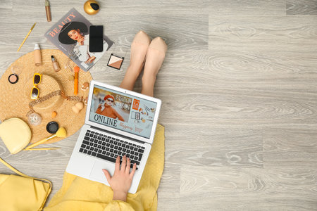 Woman with stylish accessories and decorative cosmetics using laptop for online shopping on gray wooden floorの写真素材