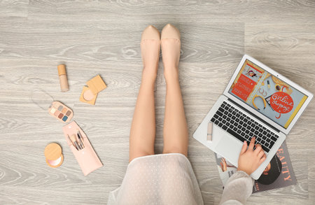 Woman using laptop for online shopping and decorative cosmetics on light wooden floorの写真素材