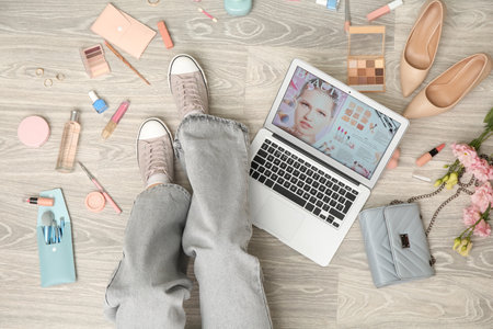 Young woman with modern laptop, accessories and decorative cosmetics on light wooden floor. Online shopping conceptの写真素材