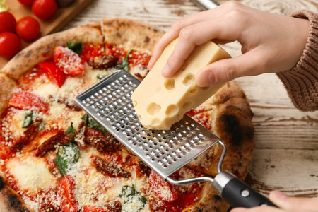 Female hands grating cheese on pizza Margarita on white wooden background. Closeupの写真素材
