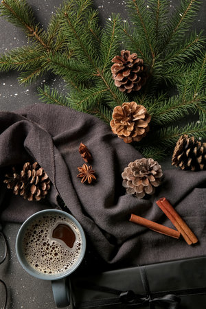 Pine cones with fir branches, cinnamon, gift box and cup of coffee on black backgroundの写真素材