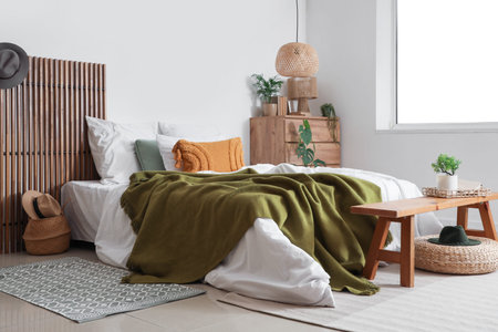 Interior of bedroom with green blanket on bed, chest of drawers and bench
