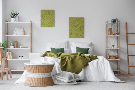 Cozy bed, shelving units and coffee table with laptop in interior of bedroom
