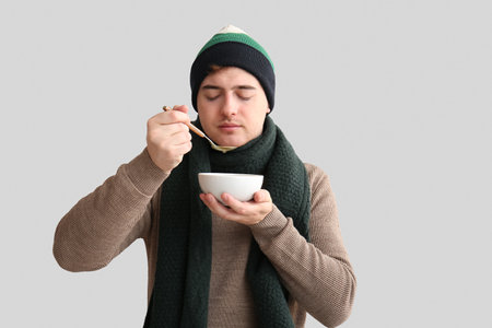 Ill young man eating soup on light backgroundの写真素材